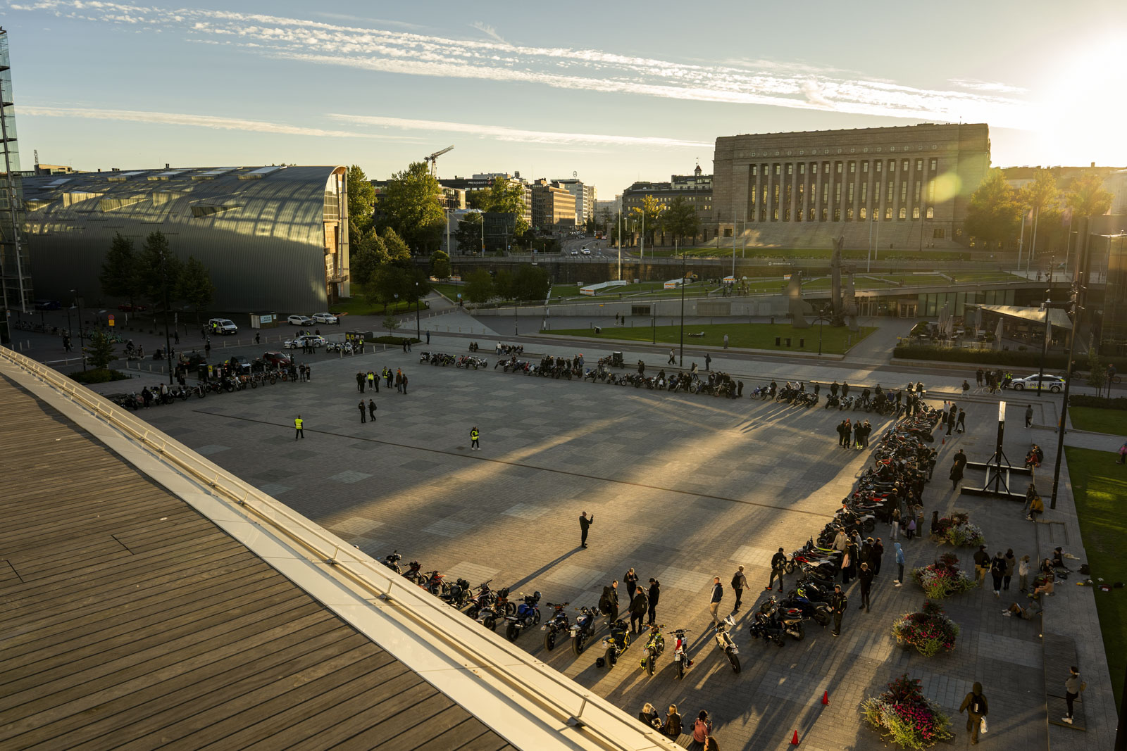 Kymmenittäin mopoja ja mopoilijoita mielenosoituksessa kansalaistorilla laskevan auringon valossa